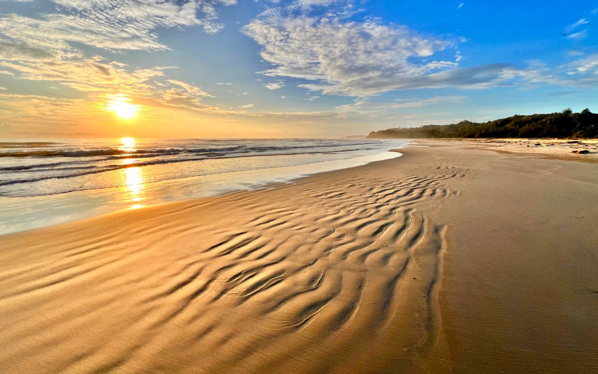 Sonnenuntergang am Strand mit Spuren im Sand (Symbolbild)